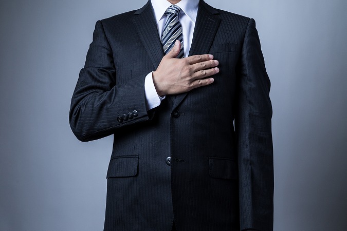 胸に手を当てるストライプネクタイの人